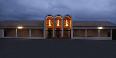 Exterior view of a building with arched entryways, lit with soft interior light, against a dark sky.