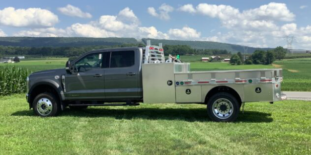 Gray utility truck parked on grass in a field under a cloudy sky