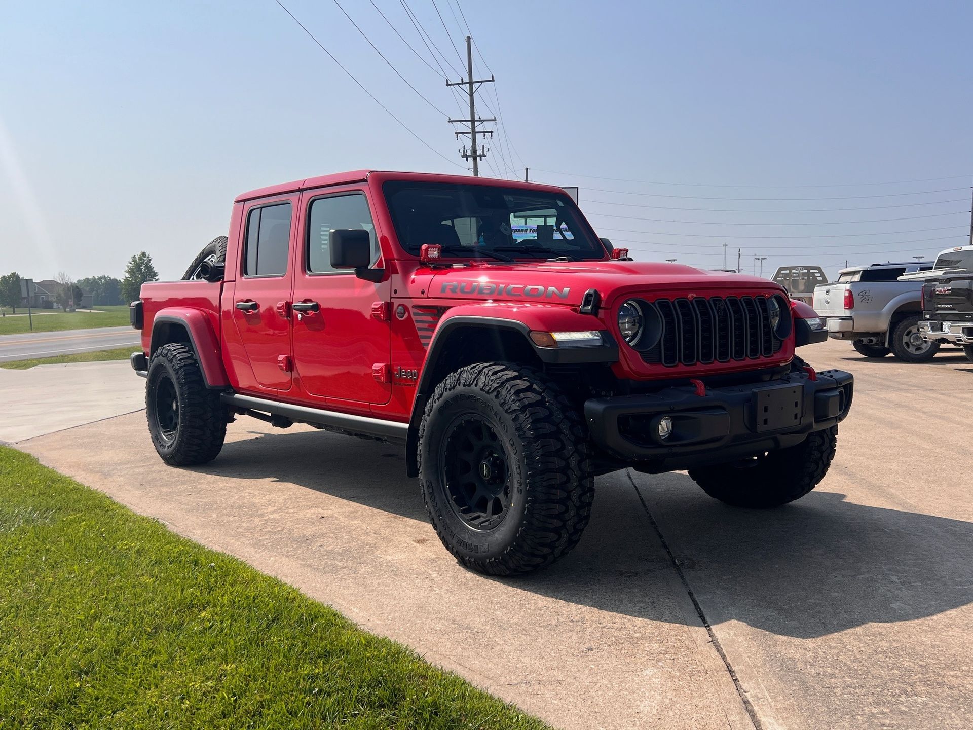 Red Jeep Wrangler parked on a roadside under a clear sky, viewed from the front-left.