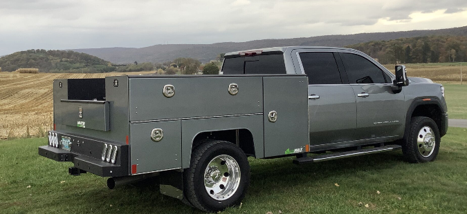 Gray pickup truck with a green utility service body parked on grass in a rural field