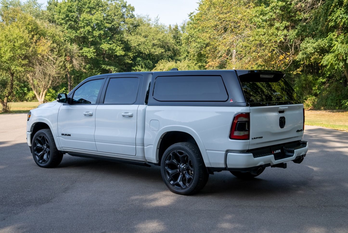 White pickup truck with a black topper parked on asphalt, trees in the background.