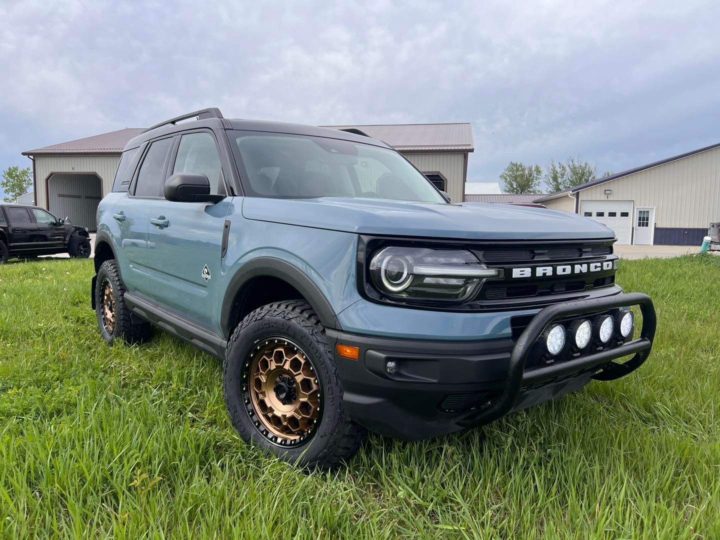 A light blue Ford Bronco Sport SUV parked on a grassy field, with black accents, bronze-colored rims, and a black bull bar with lights.