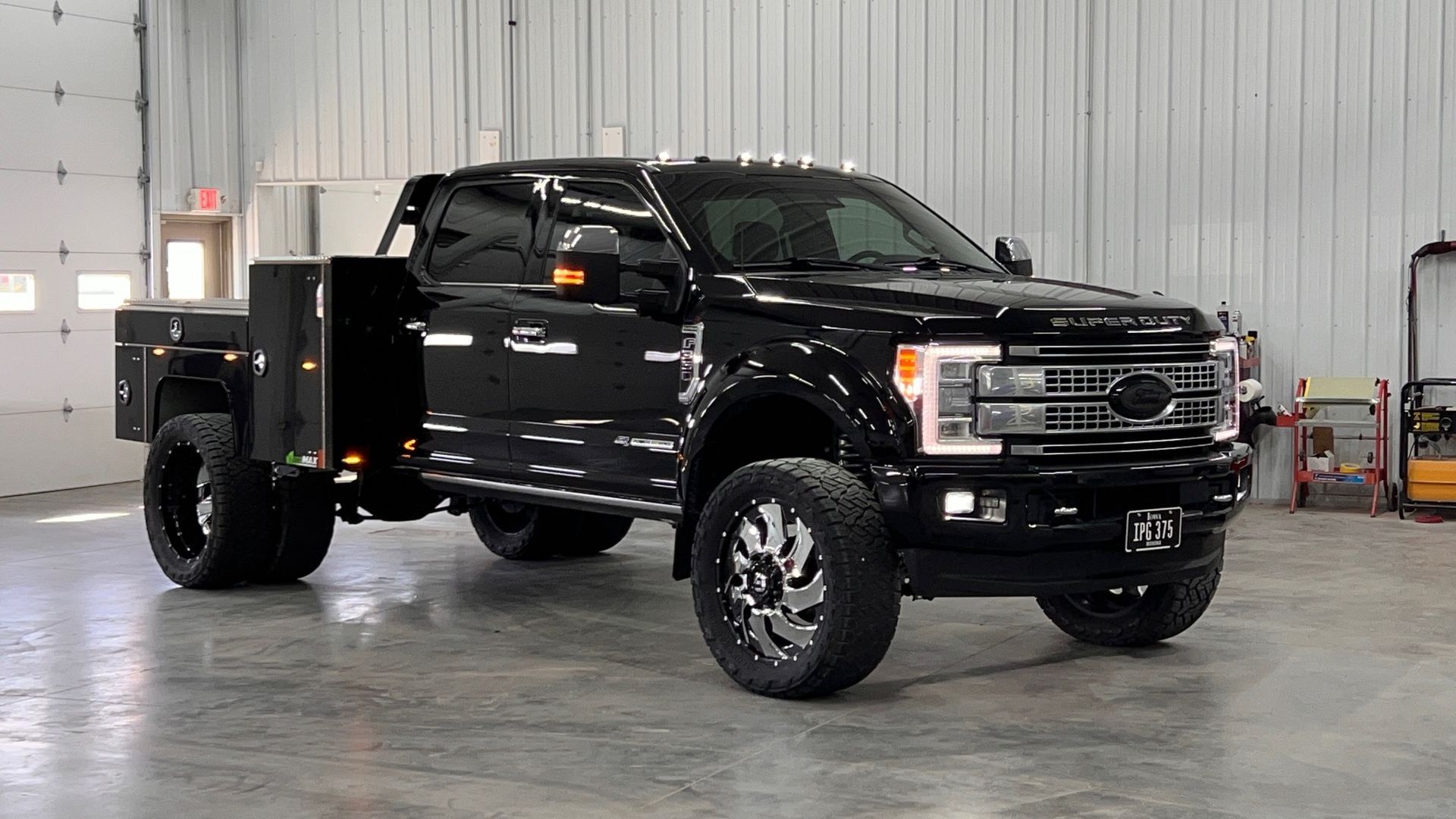 Black Ford truck with custom bed and large wheels, parked inside a garage.