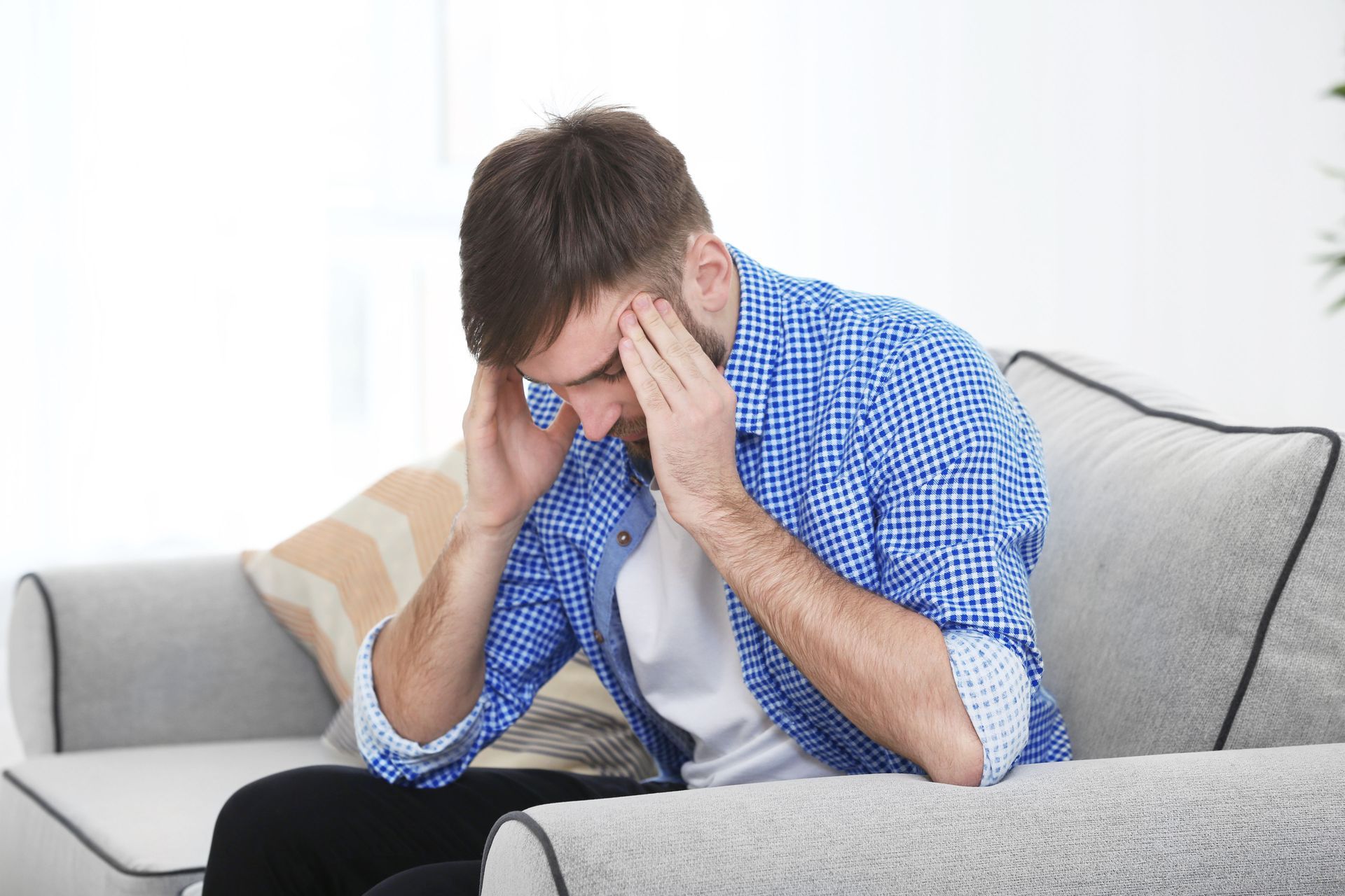Man sitting on couch, holding his head, looking stressed.