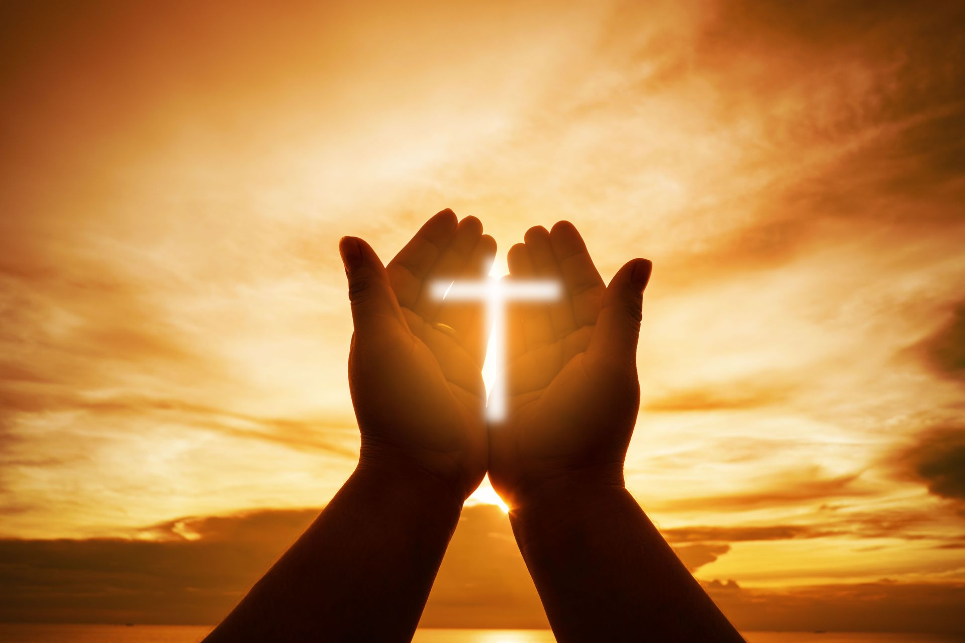 A person is holding a cross in their hands in front of a sunset.