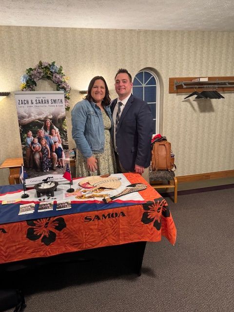 A man and a woman are standing in front of a table with a samoa flag on it.