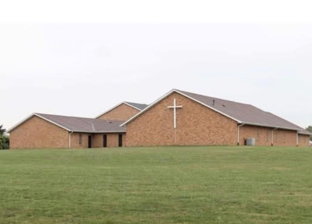 A church with a cross on the roof is in the middle of a grassy field.