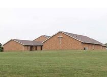 A church with a cross on the roof is in the middle of a grassy field.