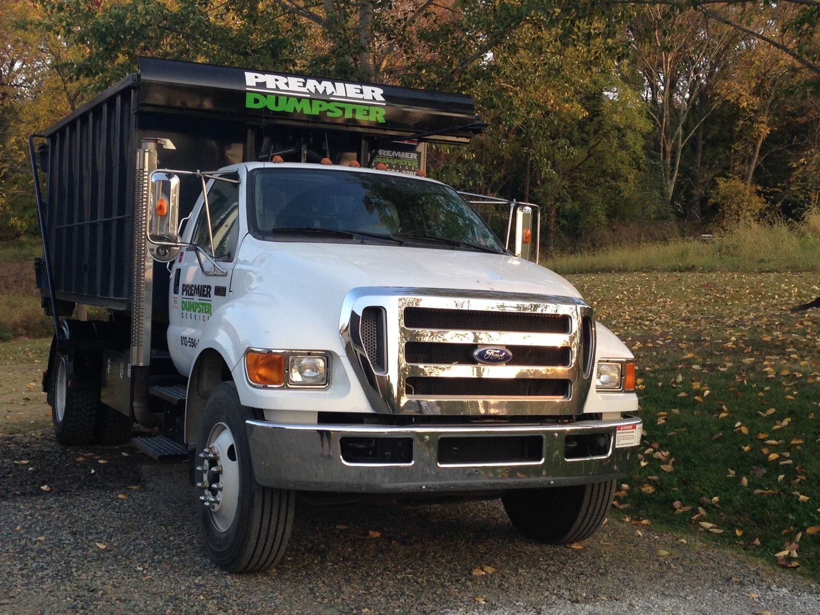 A ford dumpster truck is parked on a gravel road