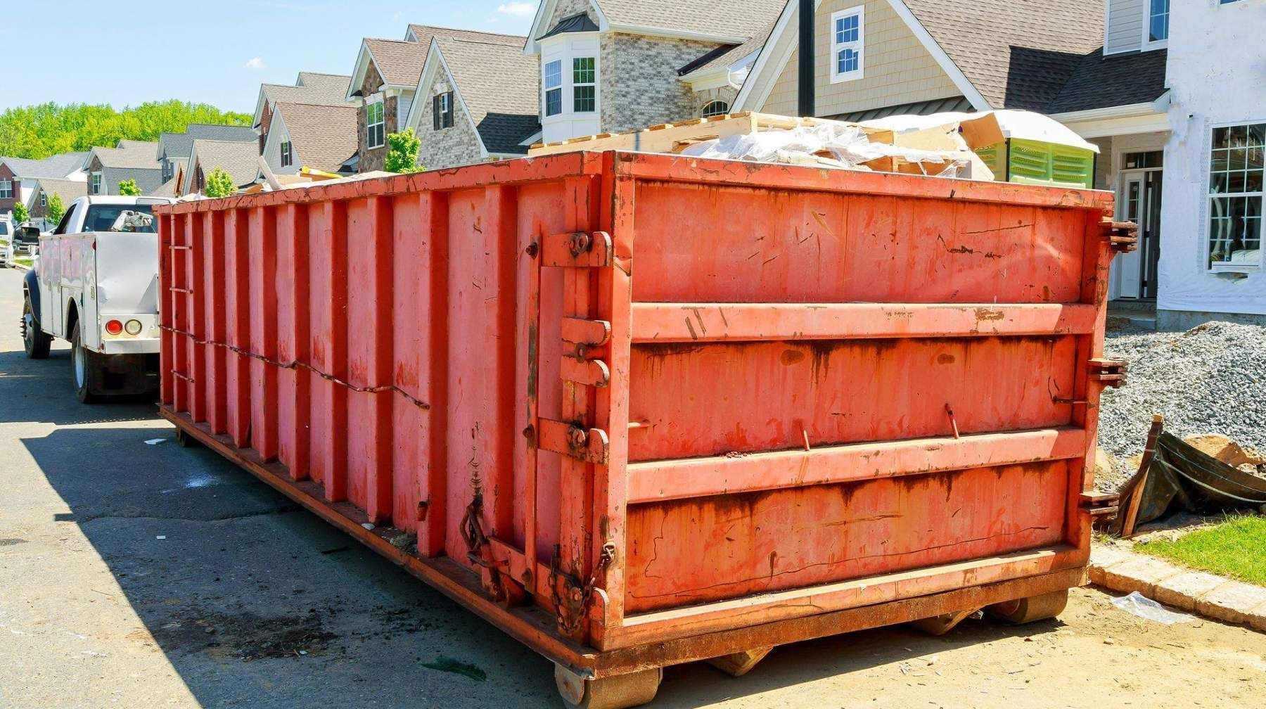 A large red dumpster is parked on the side of the road in front of a house.