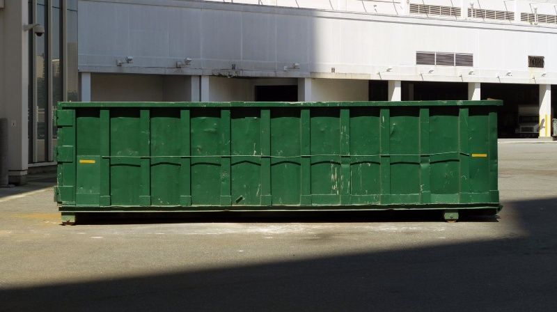 A large green dumpster is sitting in a parking lot in front of a building.