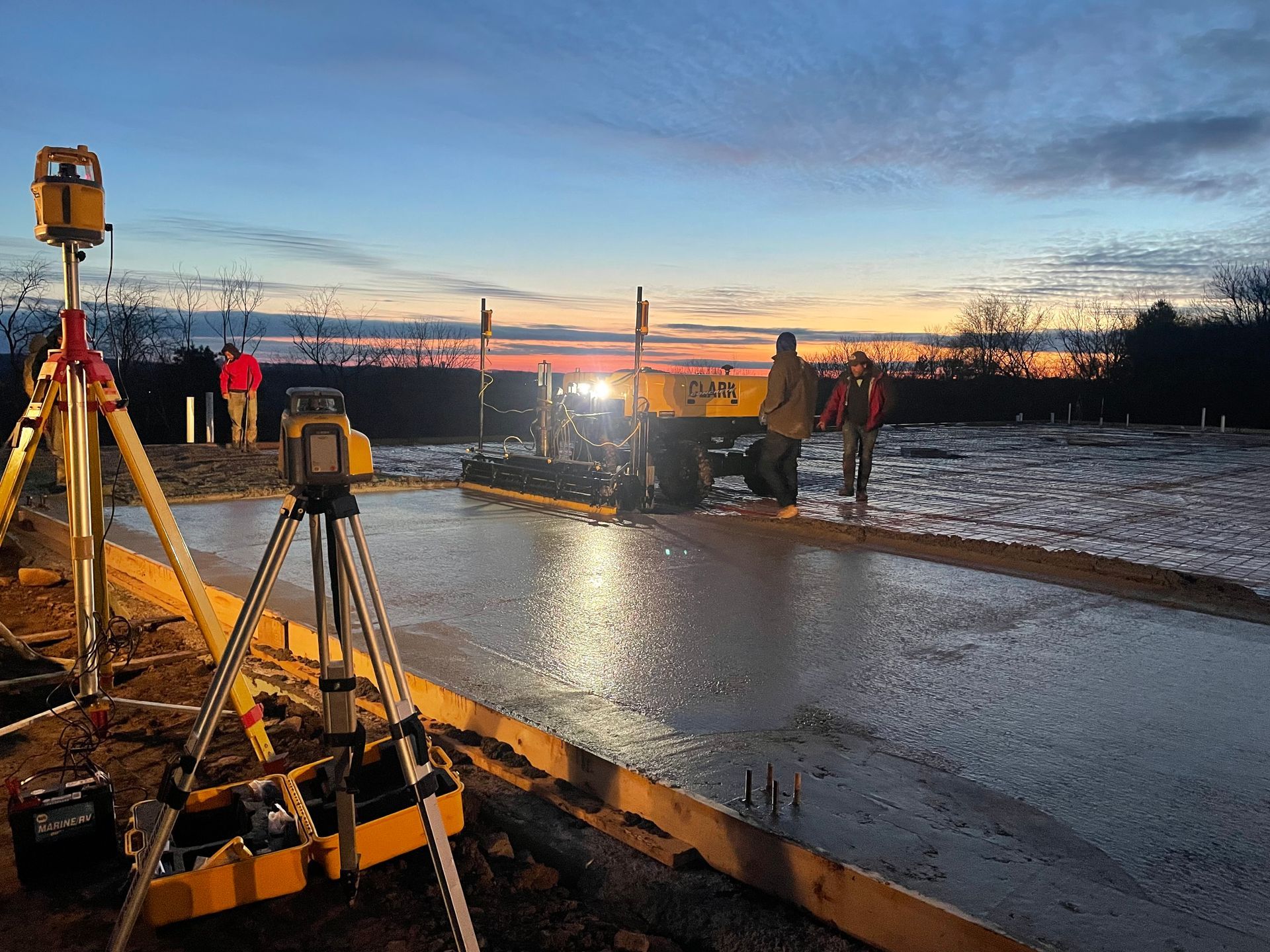 A construction site with a lot of equipment and a sunset in the background.