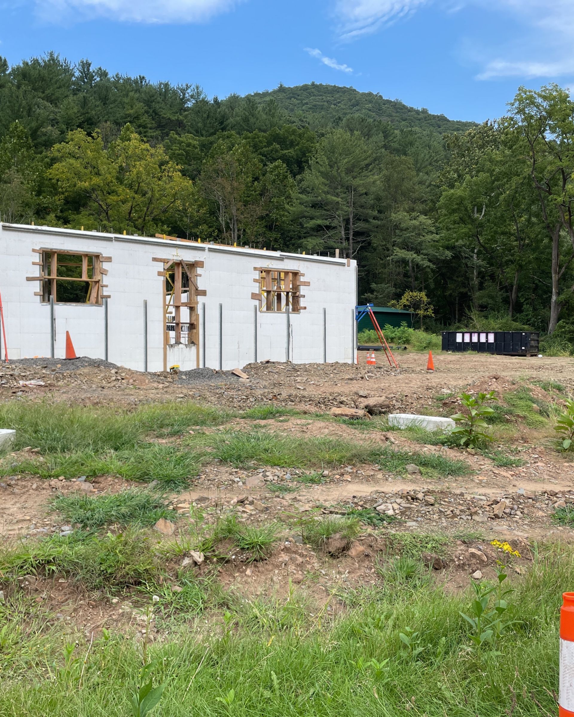 A large white building is being built in a field with trees in the background.