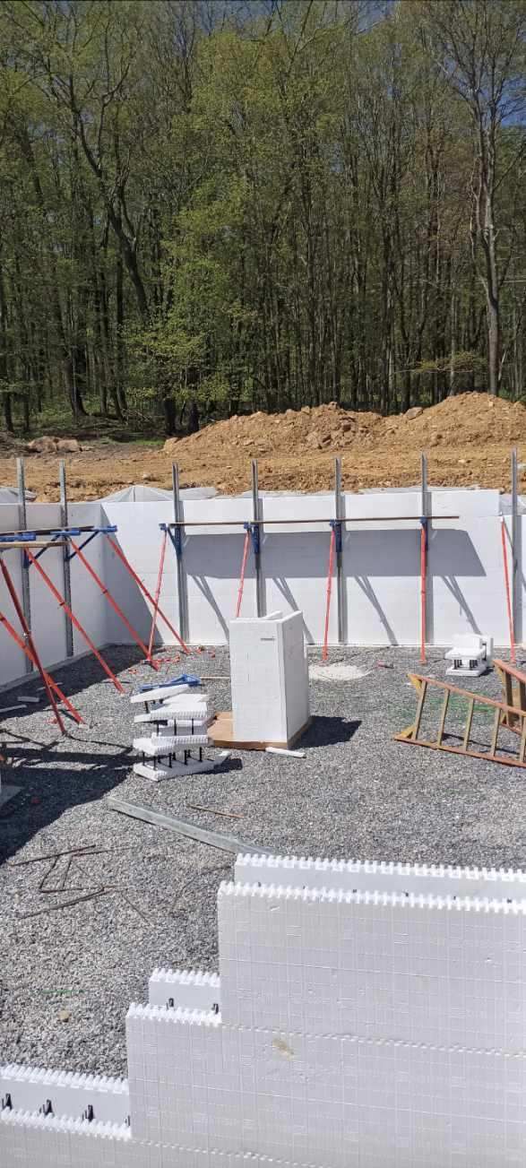 A house is being built on a gravel lot in the woods.