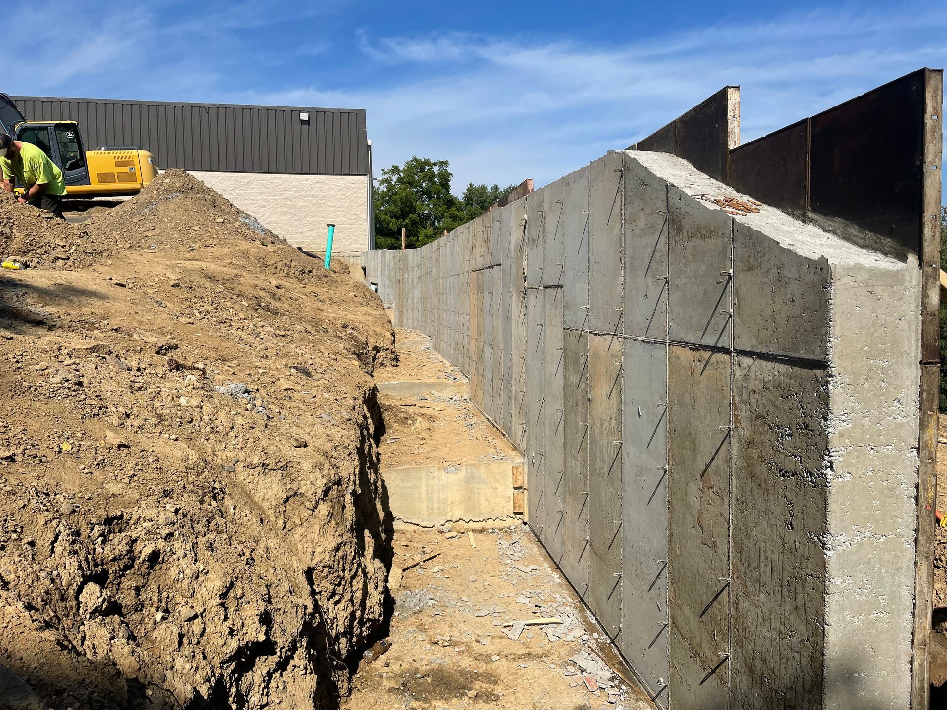 A large concrete wall is being built next to a large pile of dirt.