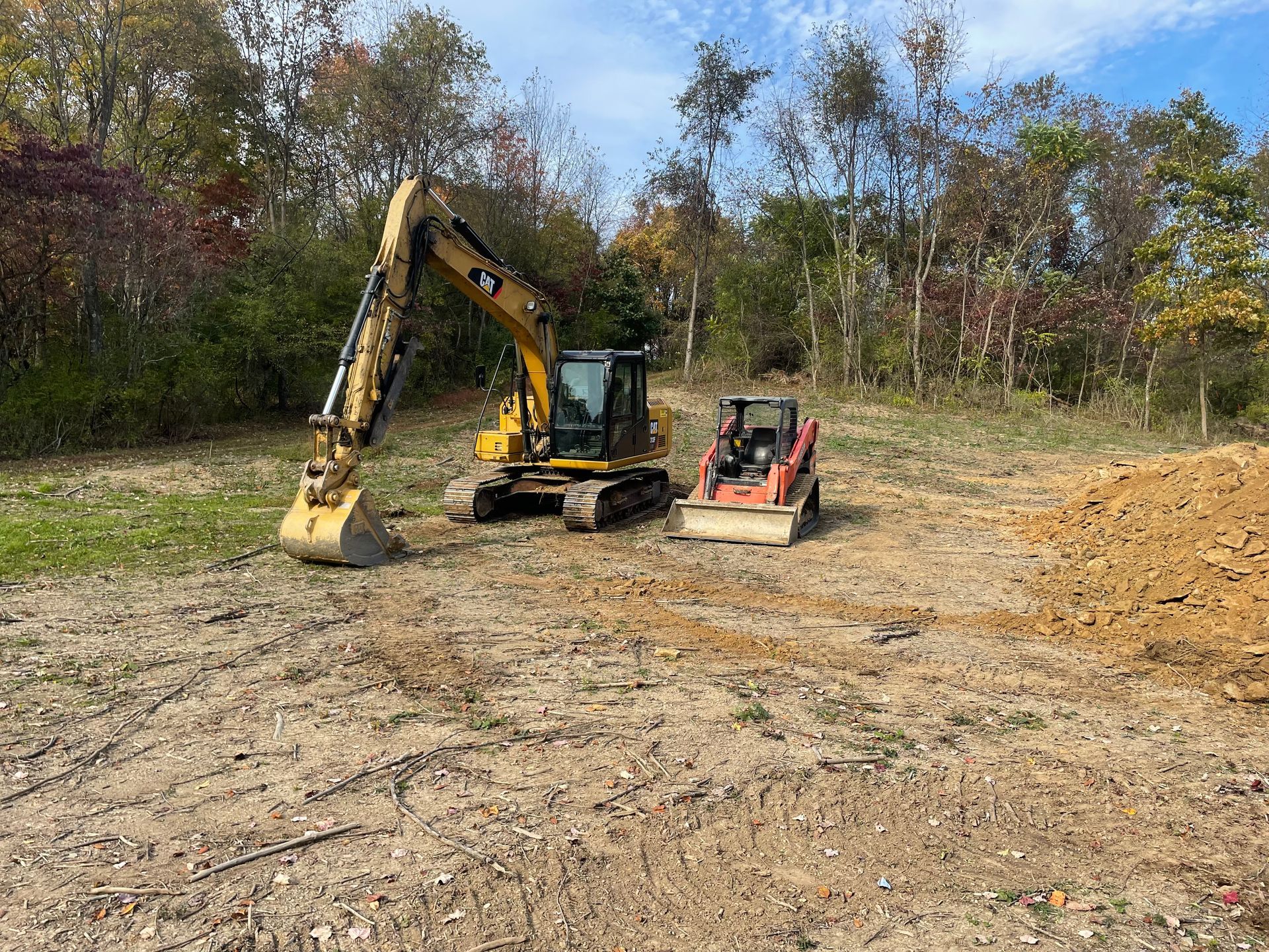 A yellow excavator and a red skid steer are parked in a dirt field.