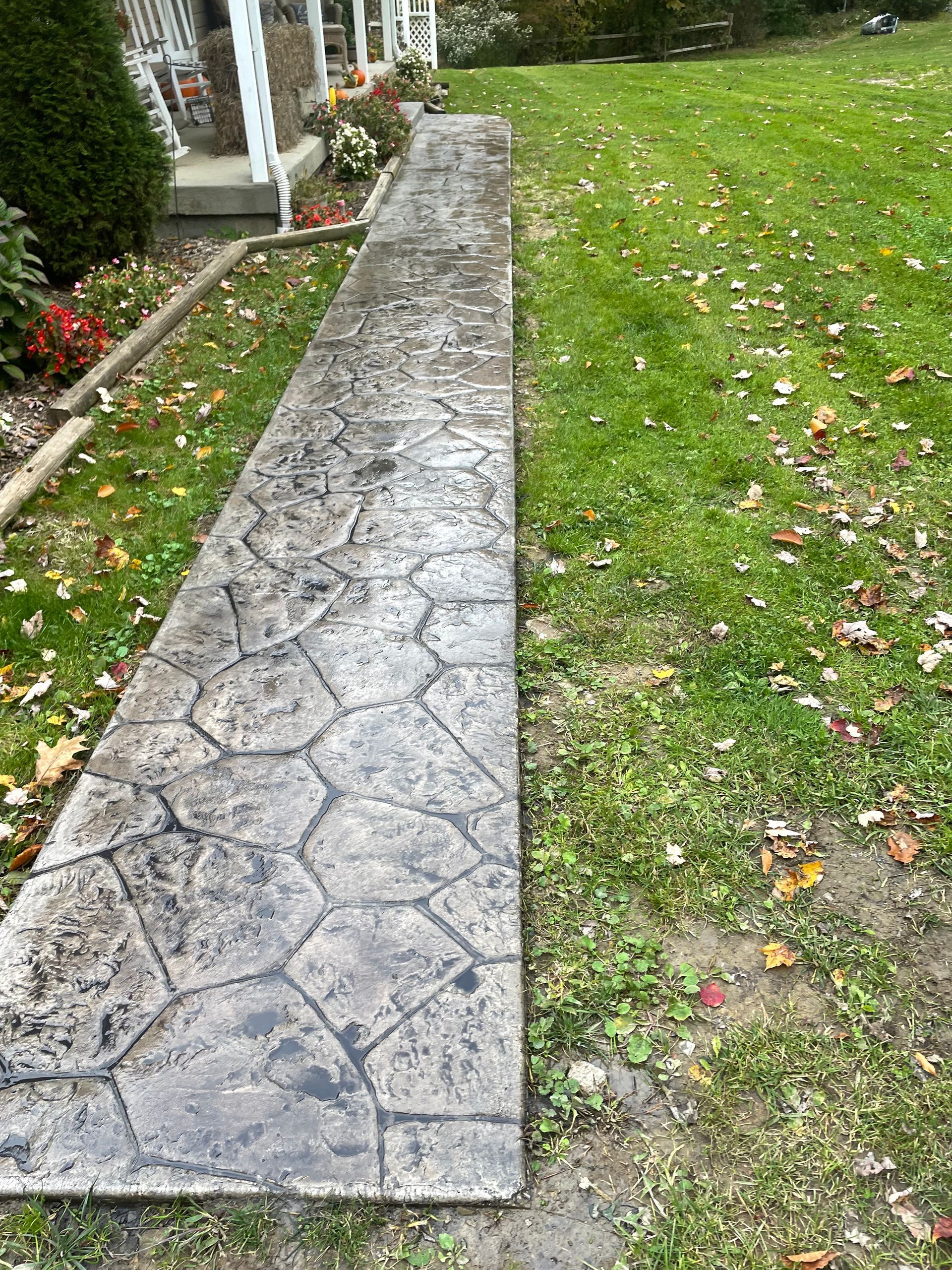 A concrete walkway leading to a house in a grassy yard.