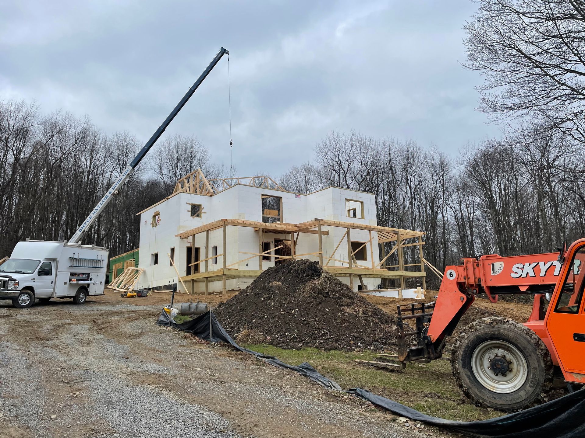 A construction site with a crane and a forklift in front of a house under construction.