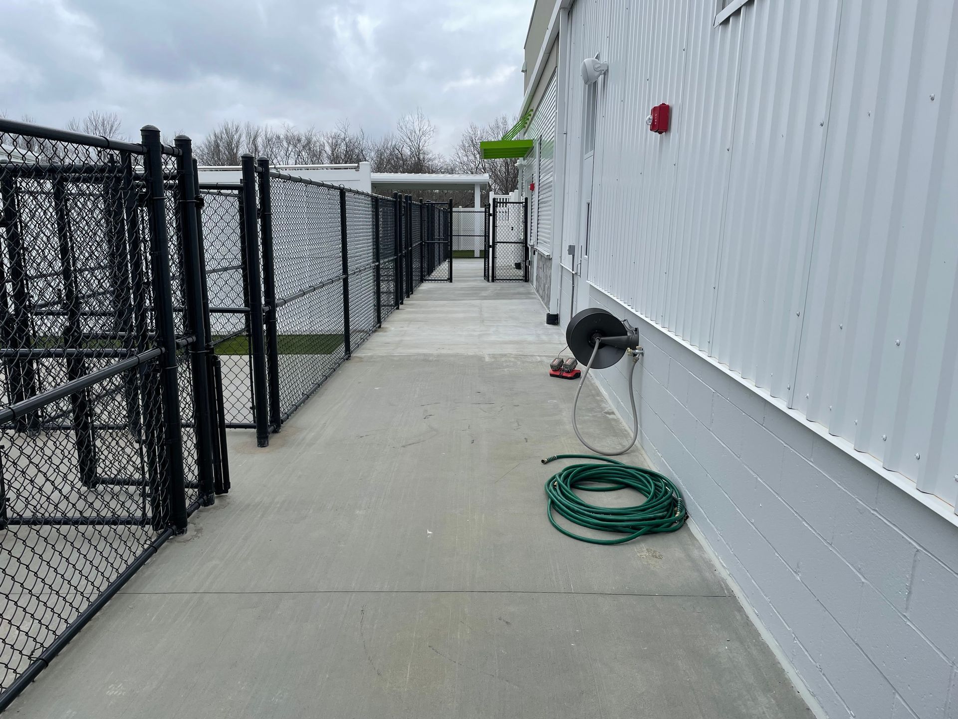 A hose is hanging on the side of a building next to a chain link fence.