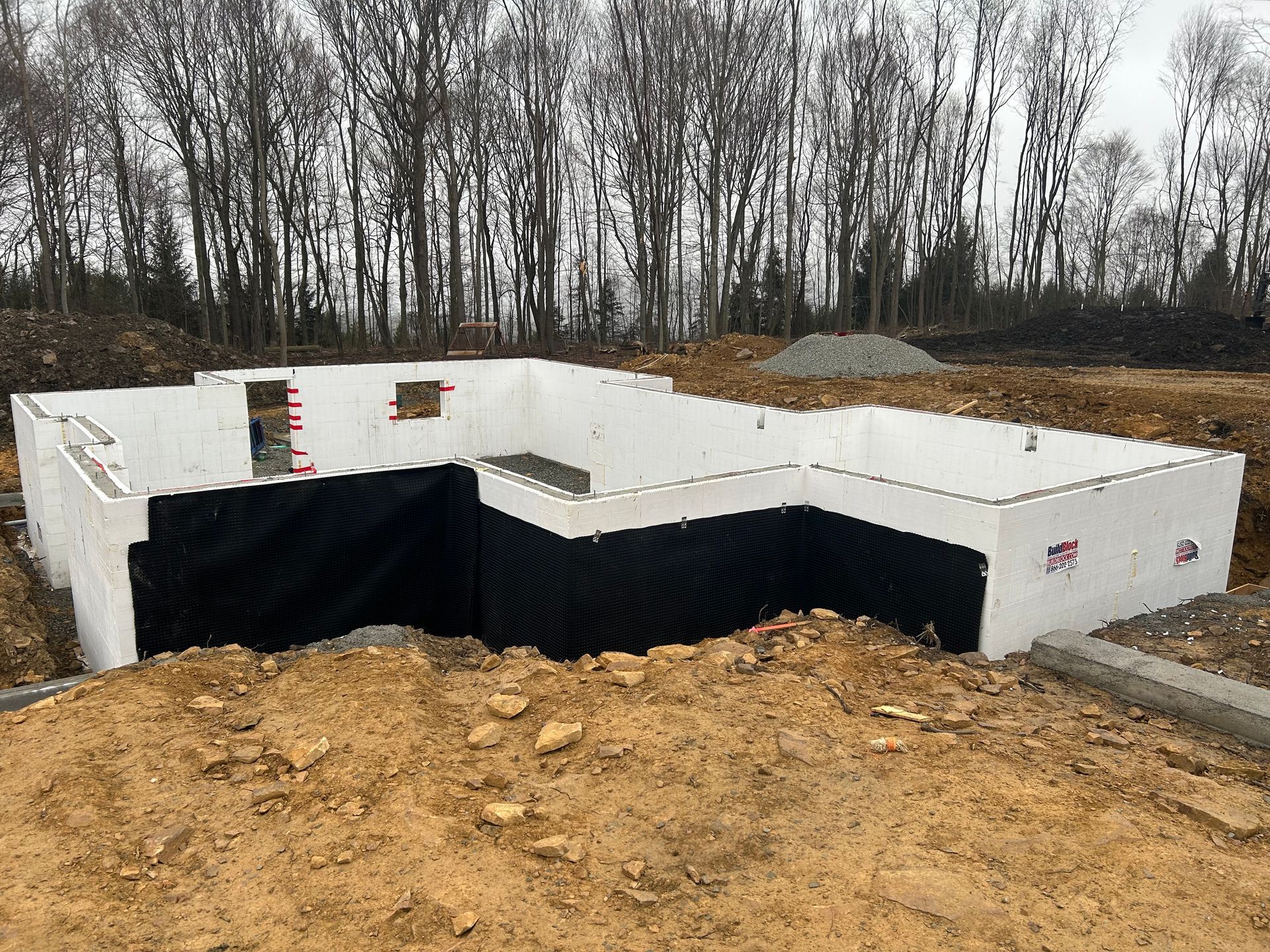 A foundation for a house is being built in a dirt field with trees in the background.