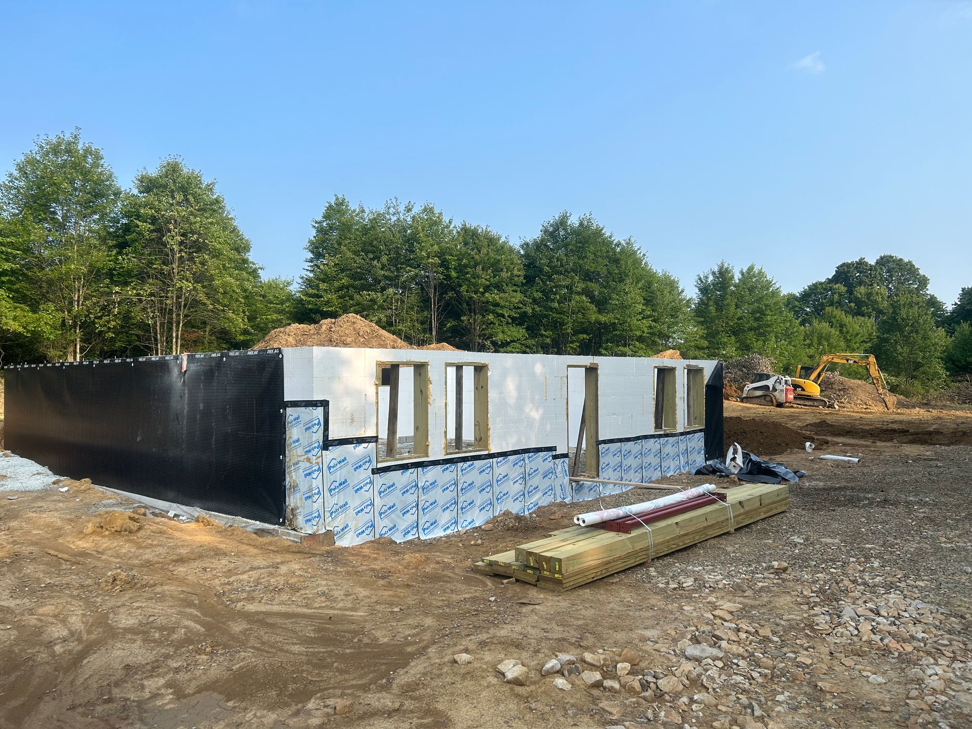 A house is being built in a dirt field with trees in the background.