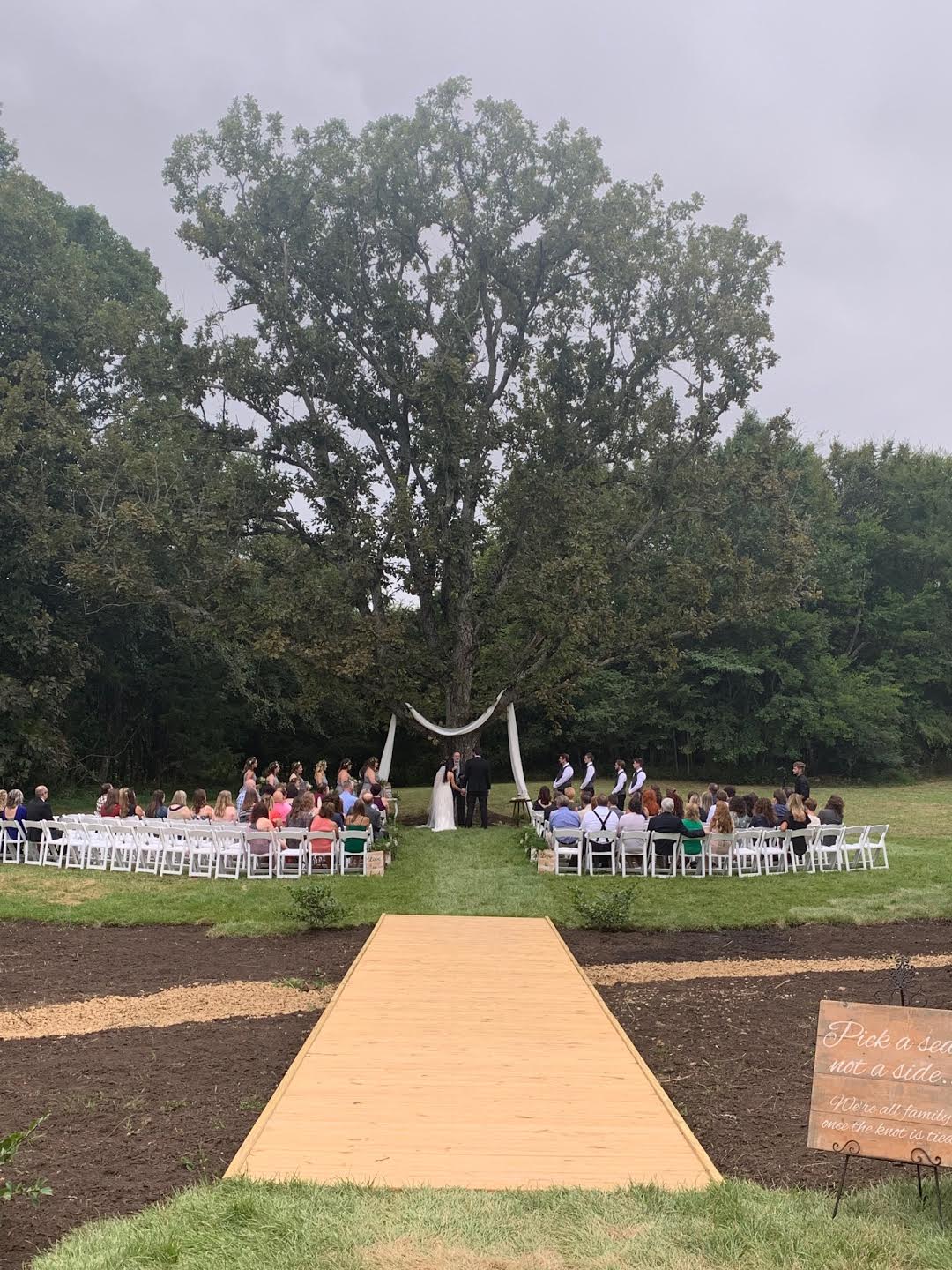 A wedding ceremony is taking place in a field with a large tree in the background.