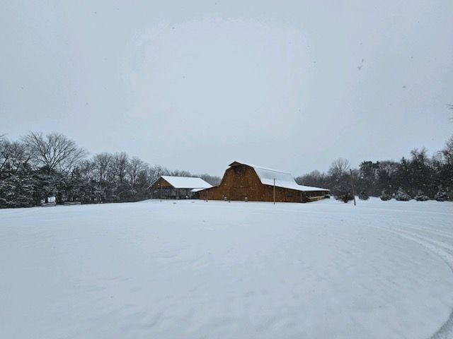 A barn is sitting in the middle of a snow covered field.