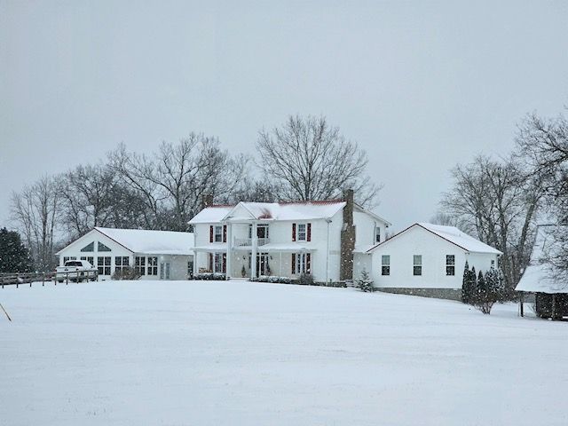 A large white house is sitting in the middle of a snow covered field.