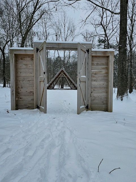 A wooden gate is surrounded by snow and trees.