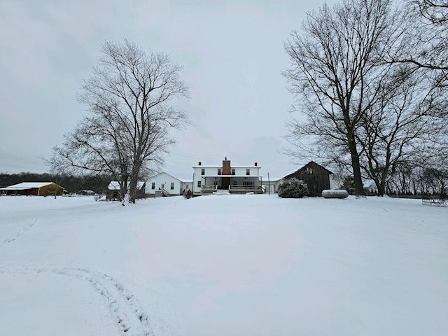 A large white house is sitting in the middle of a snow covered field.