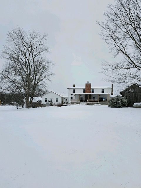 A large white house is sitting in the middle of a snow covered field.