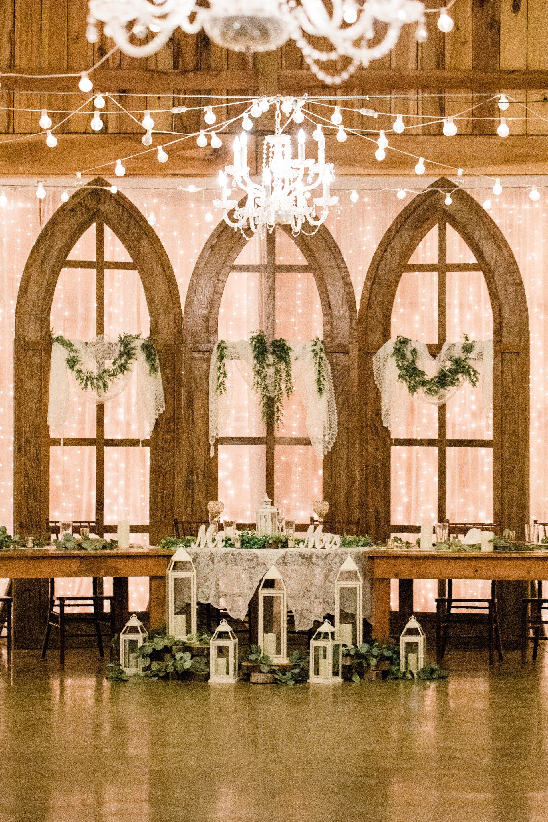 A large room with a table and lanterns in front of arched windows.