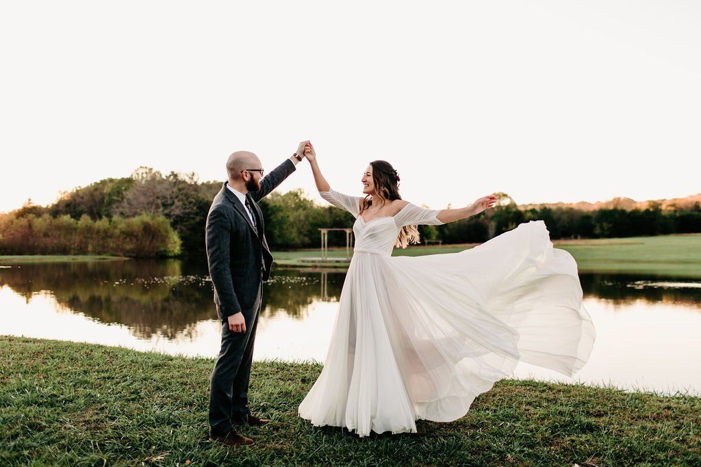 A bride and groom are dancing in front of a lake.