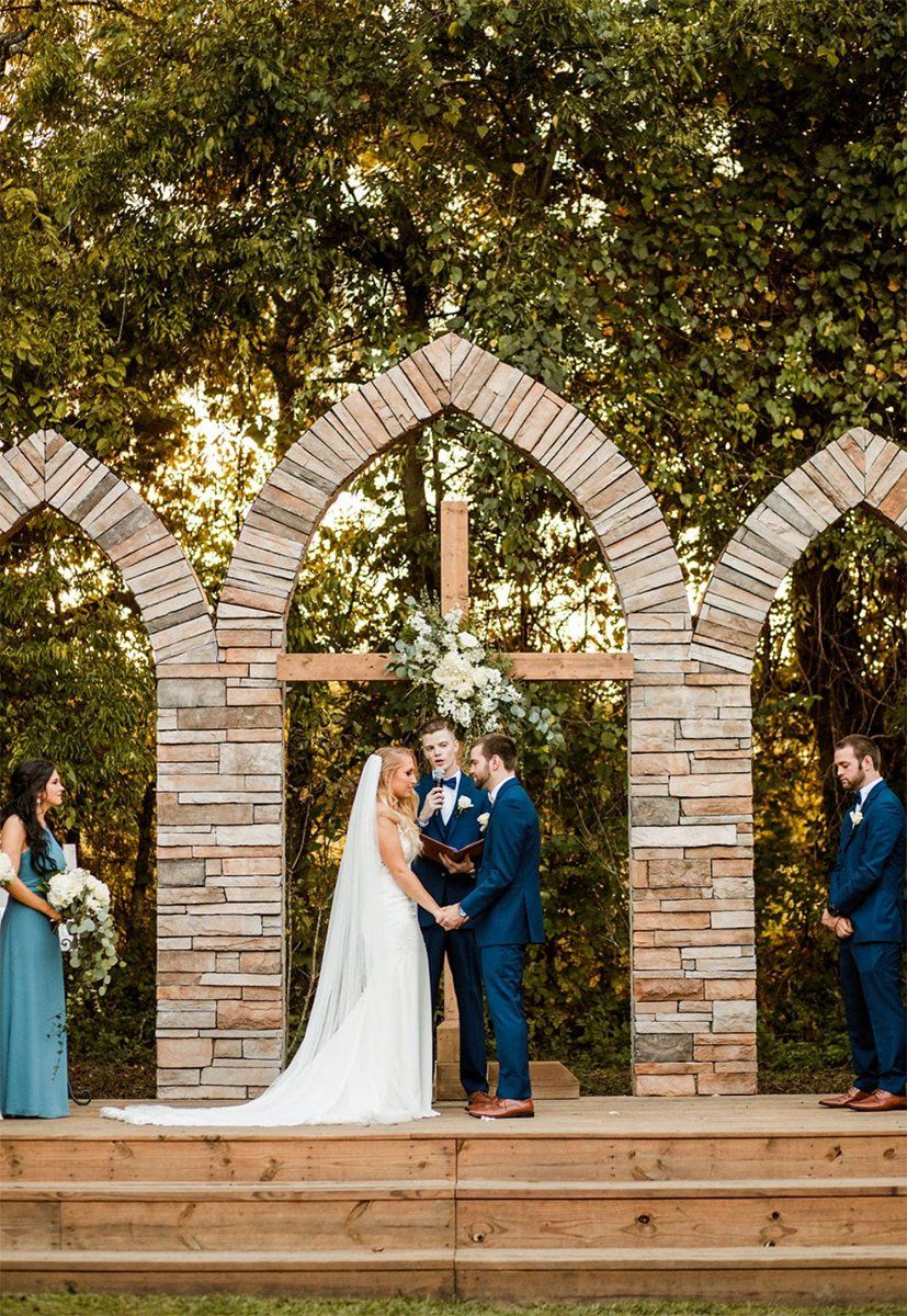 A bride and groom are holding hands during their wedding ceremony under a stone archway.