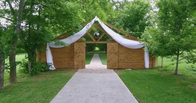 A wooden barn with a path leading to it is surrounded by trees.