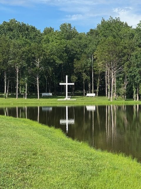 A white cross is in the middle of a lake surrounded by trees.
