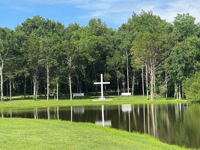 A white cross is in the middle of a lake surrounded by trees.
