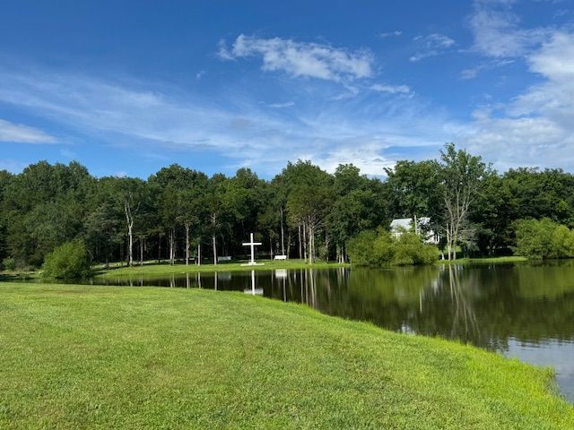 A lake surrounded by trees and grass with a cross in the middle of it.