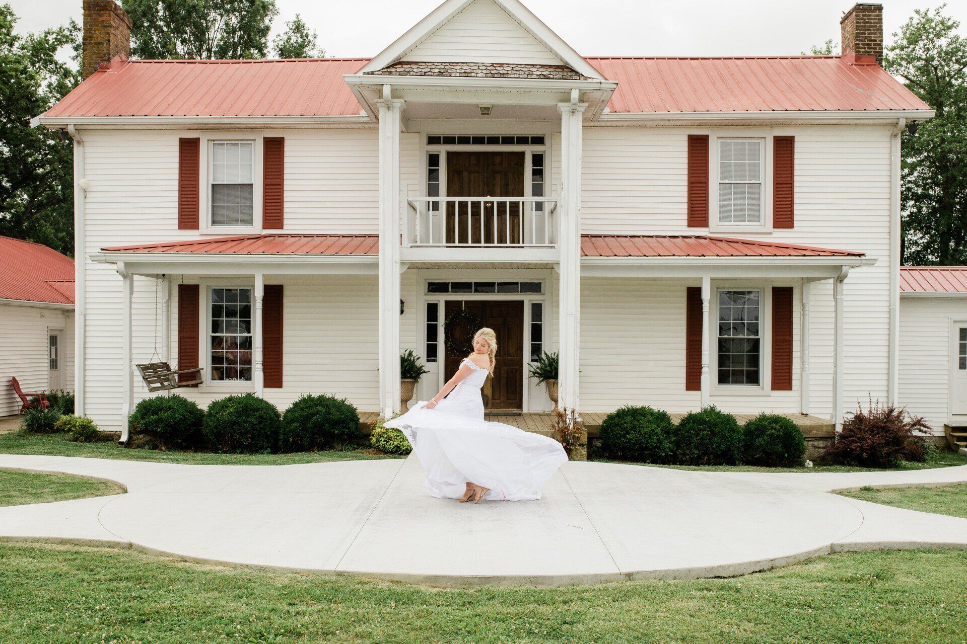 A woman in a wedding dress is standing in front of a large white house.