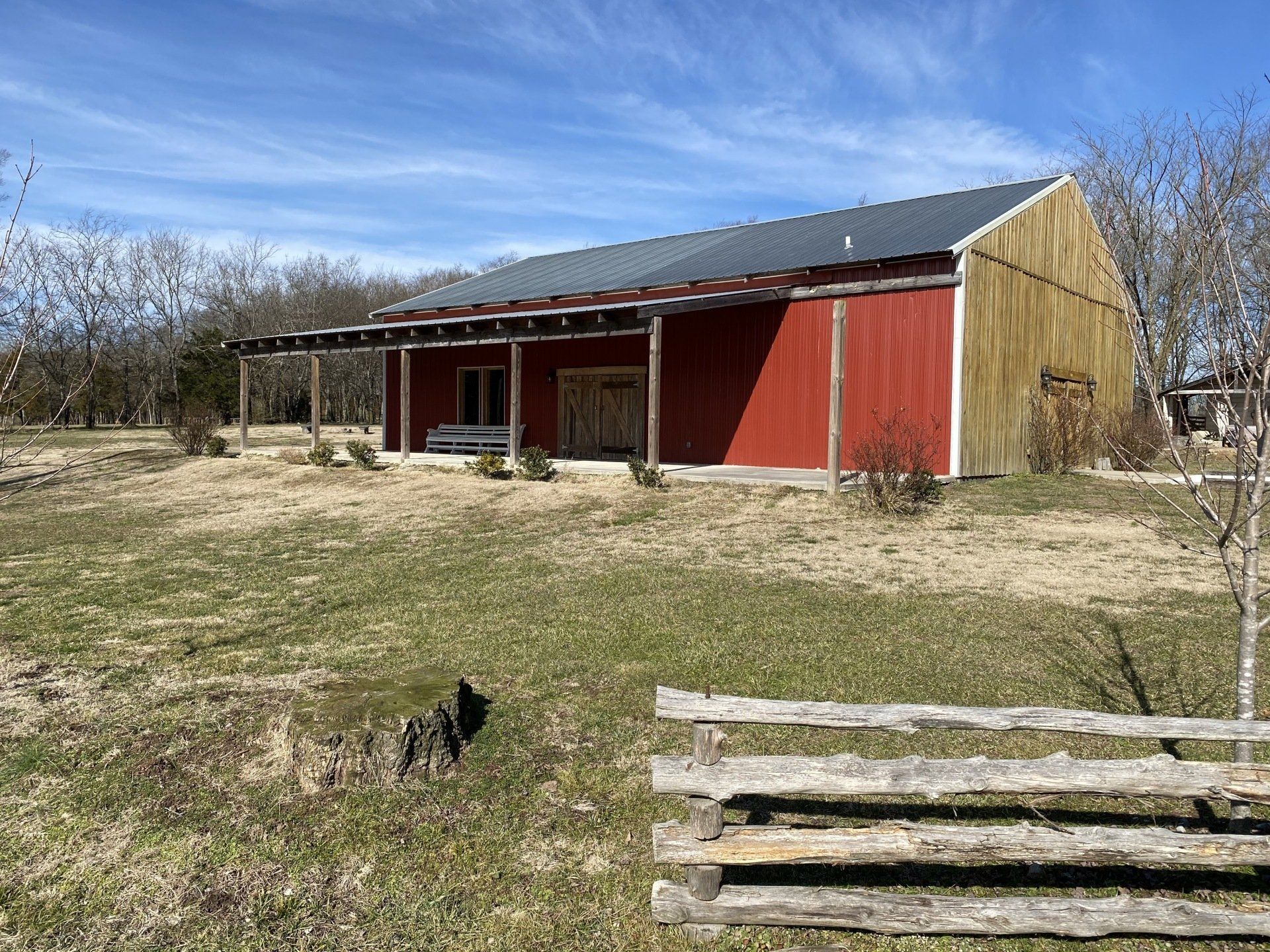 A red barn is sitting in the middle of a grassy field next to a wooden fence.