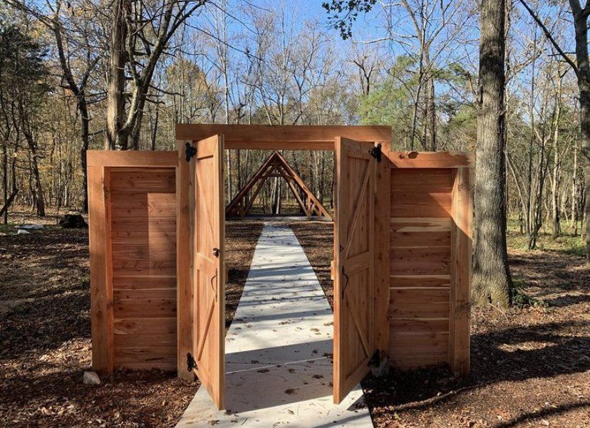 A wooden gate is open to a path in the woods.