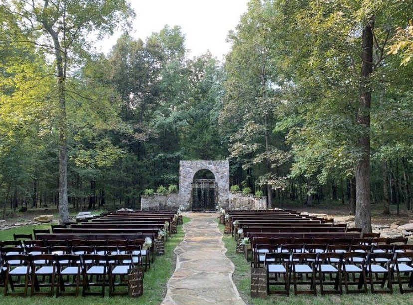 A row of wooden chairs are lined up in front of a stone archway.
