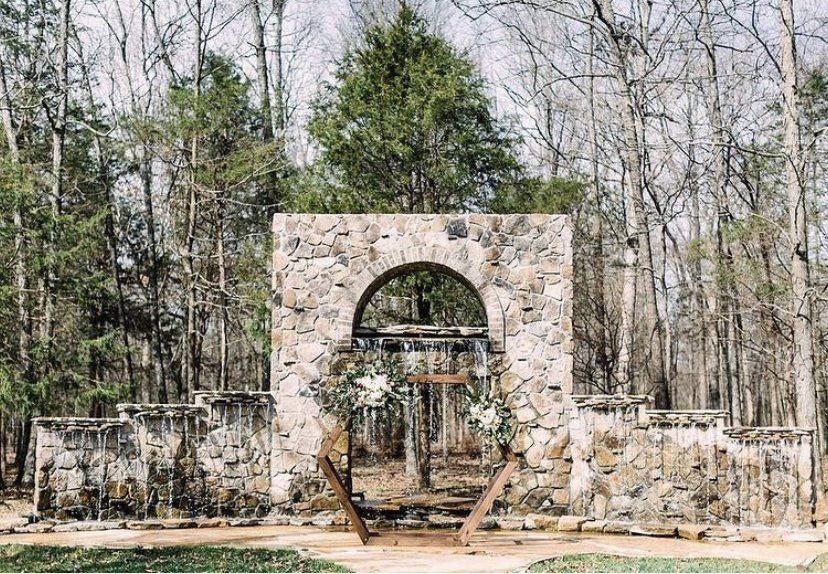 There is a stone archway in the middle of the woods.