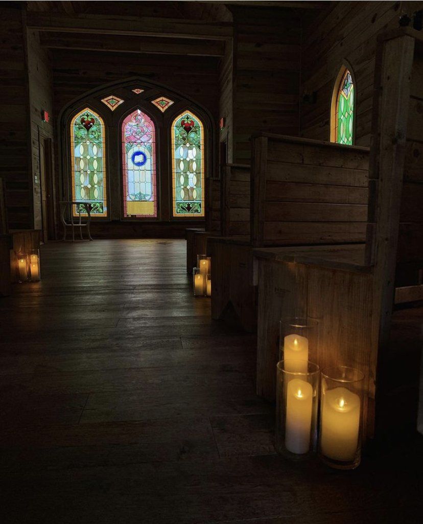 Candles are lit up in a church with stained glass windows.