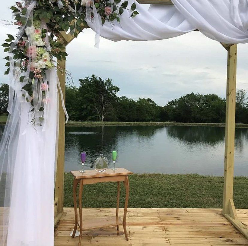 A wooden arch with flowers and a table in front of a lake