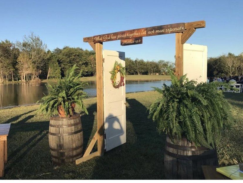 A wooden archway with ferns and barrels in front of a lake.