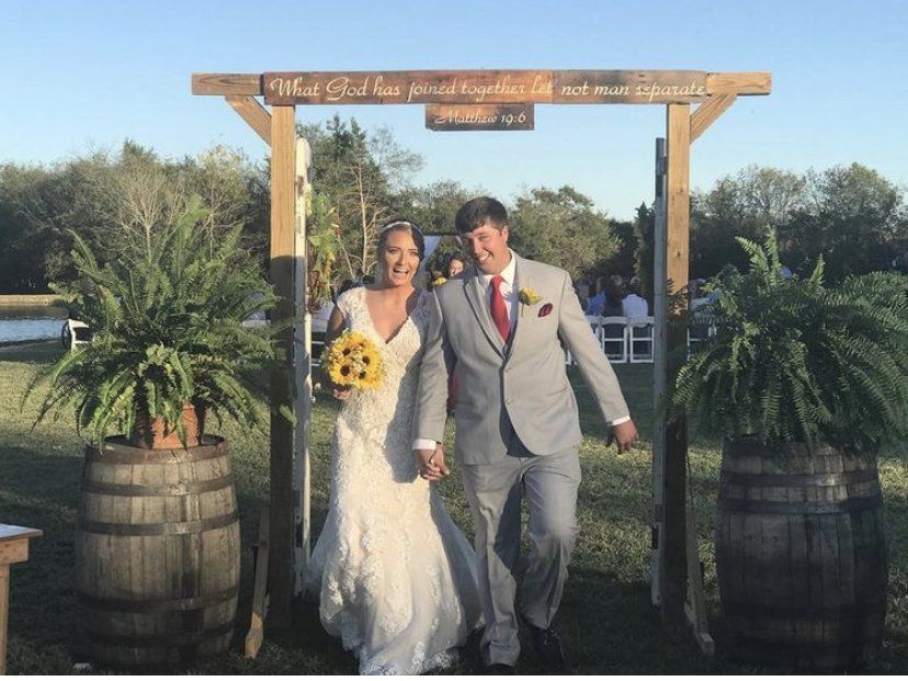 A bride and groom are walking under a wooden archway.