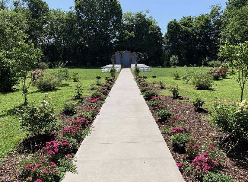A concrete walkway leading to a gazebo surrounded by flowers and trees.