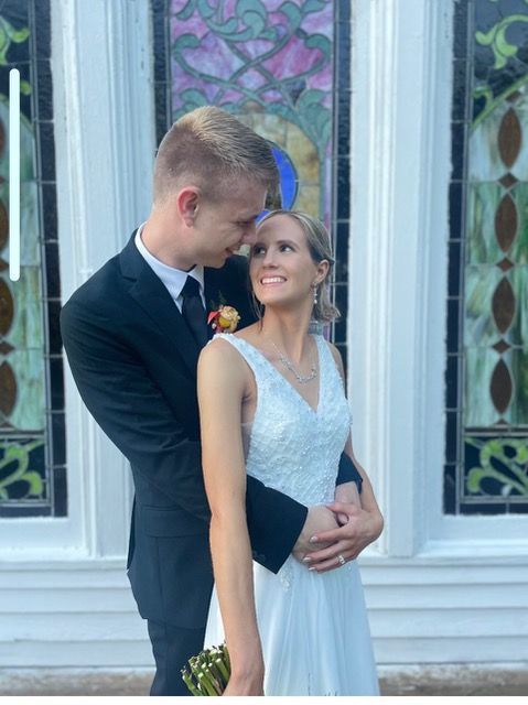 A bride and groom are posing for a picture in front of a stained glass window.