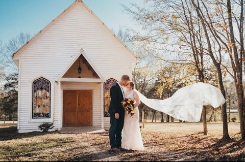 A bride and groom are posing for a picture in front of a small white church.